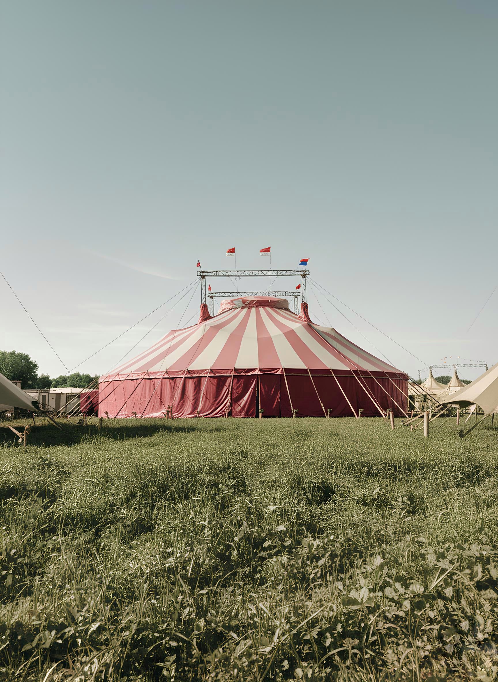 A red and white striped big-top tent standing in a grassy field