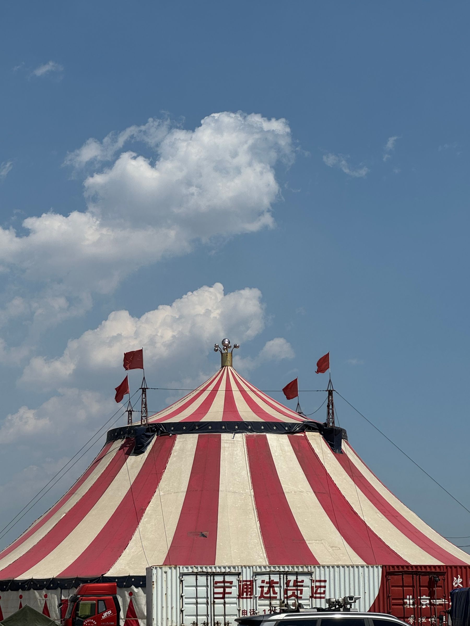 The striped peak of a circus tent with flags against the sky